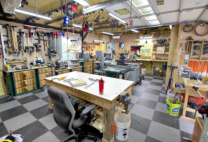 Inside of workshop. Many tools, cabinets with workbench in middle of shop.