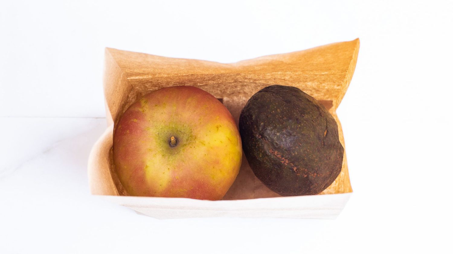 overhead view of avocado and apple in a brown paper bag