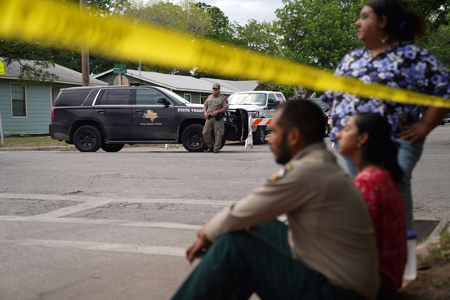 People sit on the curb outside of Robb Elementary School as State troopers guard the area in Uvalde, Texas, on May 24, 2022. - An 18-year-old gunman killed 14 children and a teacher at an elementary school in Texas on Tuesday, according to the state's governor, in the nation's deadliest school shooting in years.