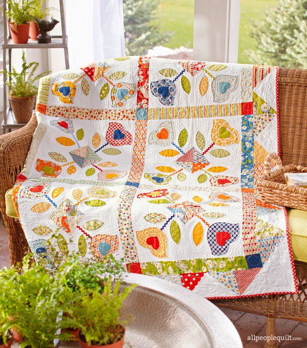 Applique quilt draped over a wicker chair with window in background 