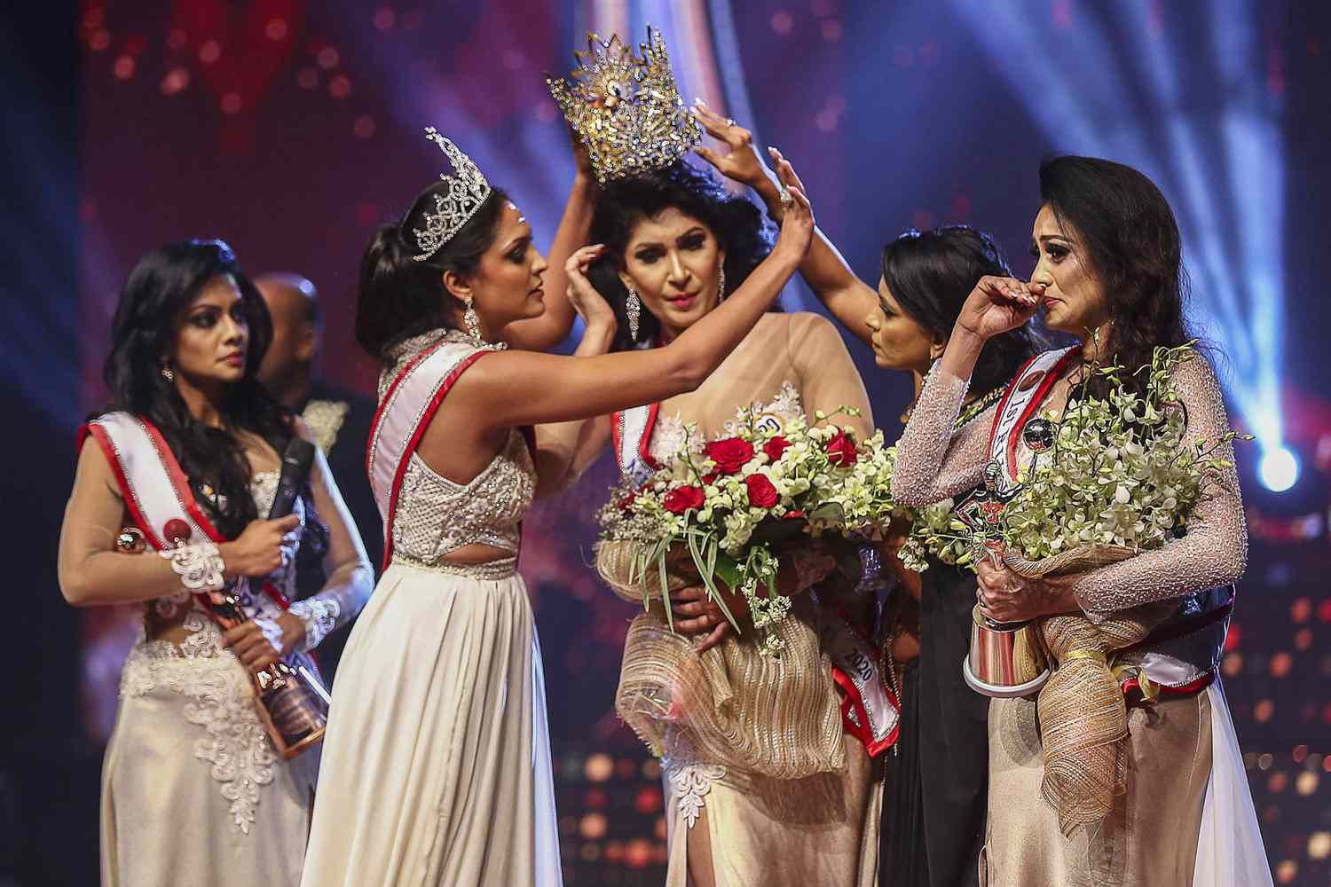 In this photograph taken on April 4, 2021, winner of Mrs. Sri Lanka 2020 Caroline Jurie (2-L) removes the crown of 2021 winner Pushpika de Silva (C) as she is disqualified by the jurie over the accusation of being divorced, at a beauty pageant for married women in Colombo