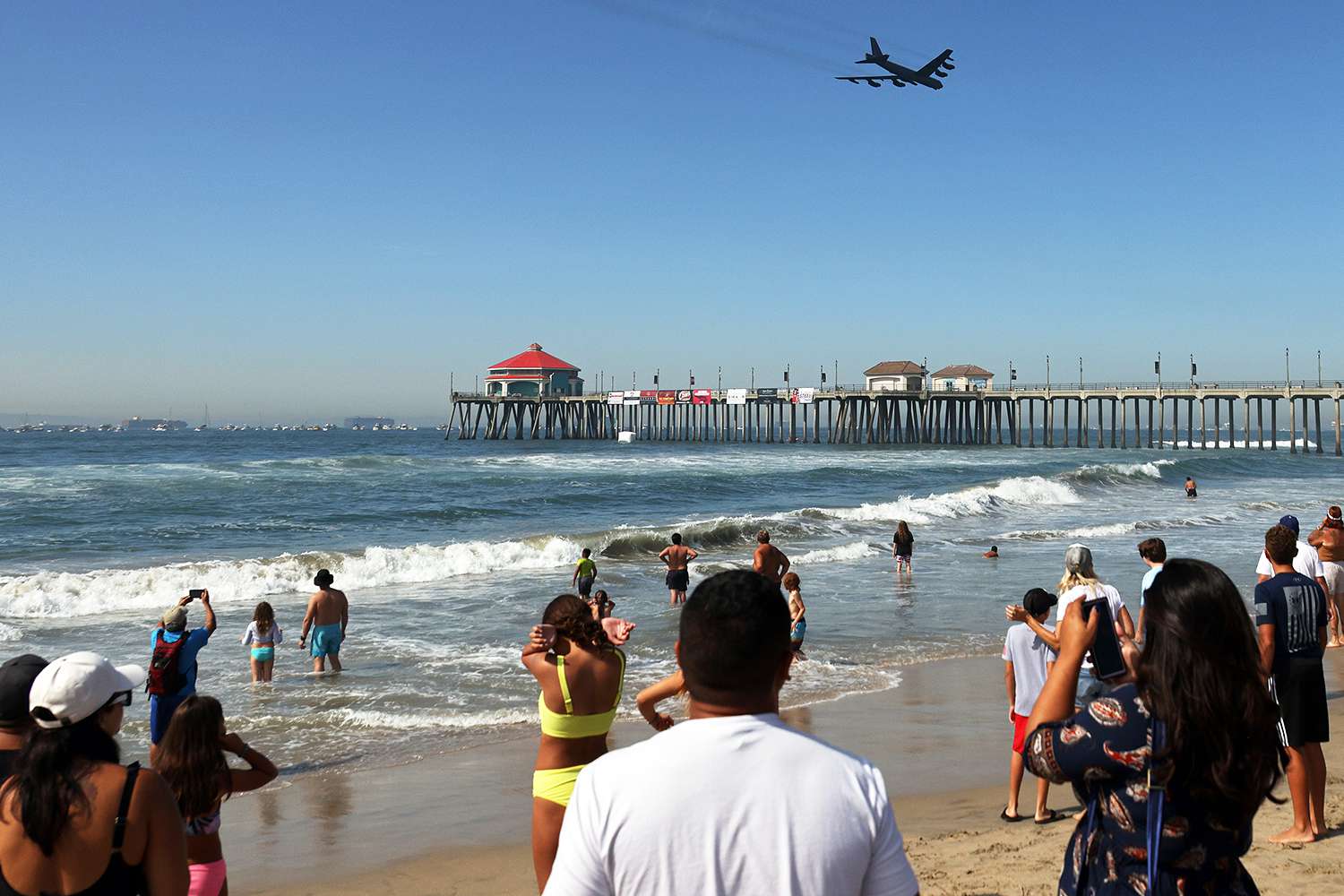 People watch as a Boeing B-52 Stratofortress flies over the Huntington Beach Pier during the Pacific Airshow on October 01, 2021 in Huntington Beach, California.