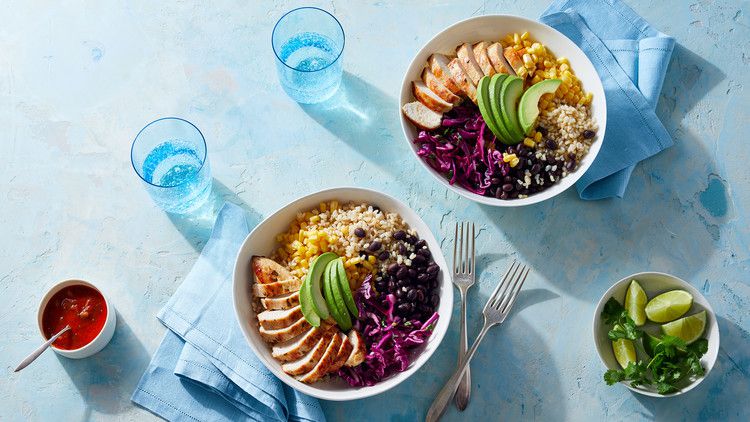 burrito bowl with avocados corn rice chiken beans and cabbage on blue table