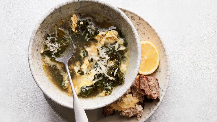 stracciatella soup with kale and lemon served in grey bowl with bread and lemon on the side