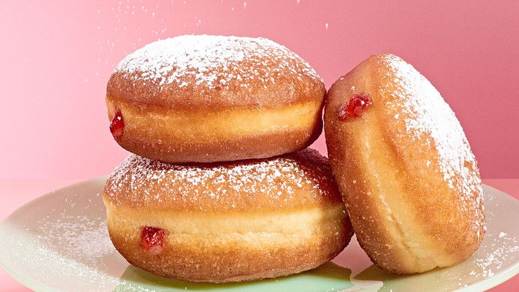 strawberry jam-filled doughnut getting sprinkled with powdered sugar