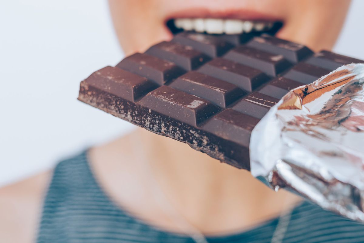 Close-up of young woman eating a chocolate bar. Happy female smiling and enjoying the dessert.