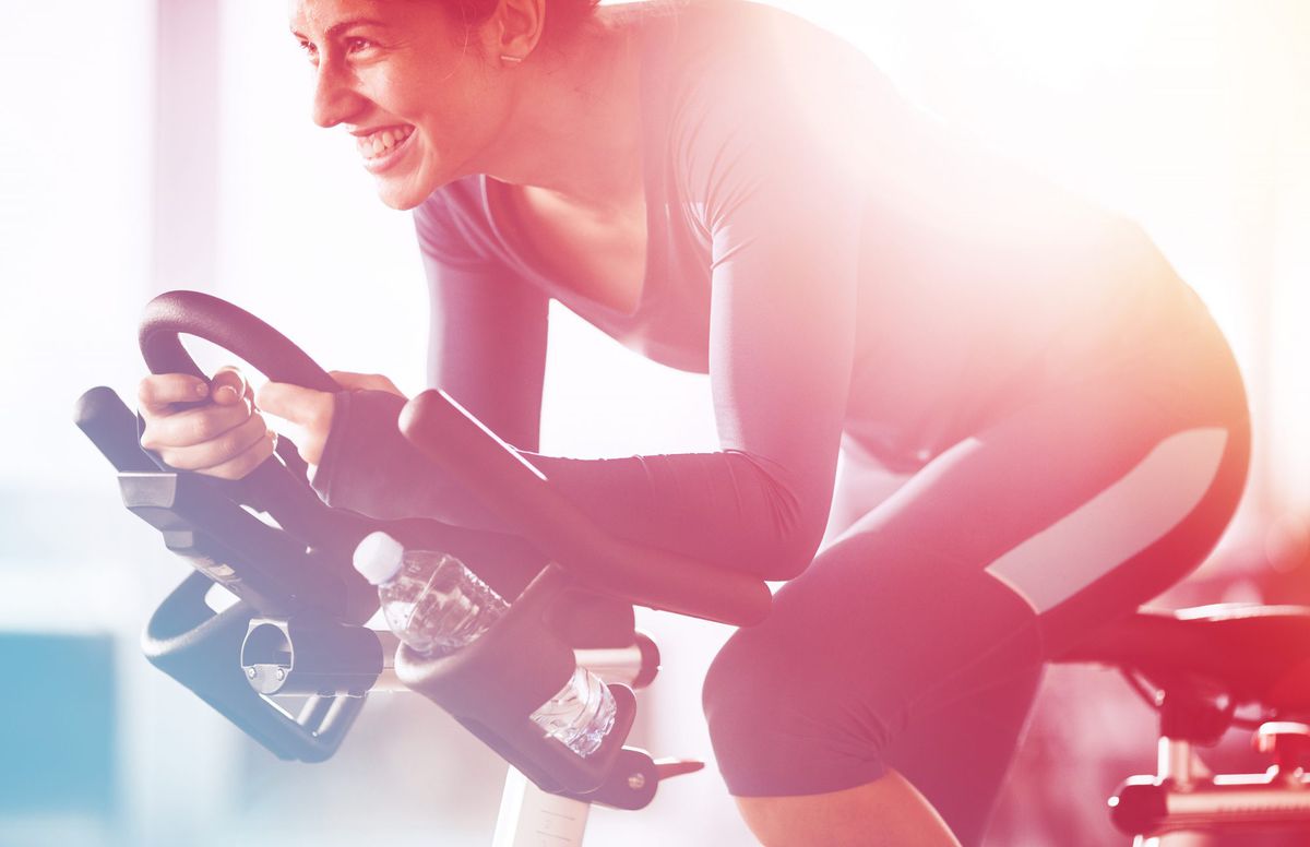Young happy sportswoman having exercising class on sports training in a health club. - Happy athletic woman cycling on exercise bike in a gym.