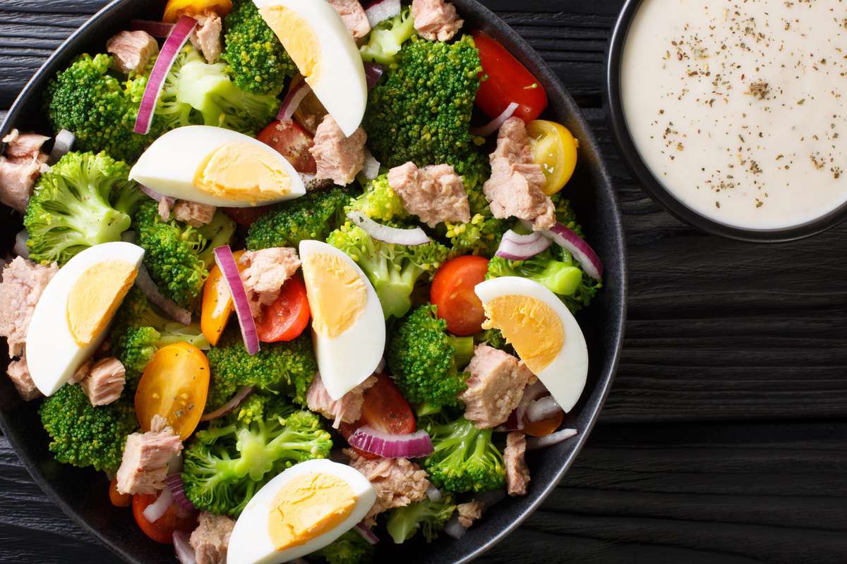 military-diet-tuna-brocoli-salad , Breakfast salad with tuna, broccoli, tomatoes, onions and eggs and yogurt dressing closeup in a plate on the table. Horizontal top view from above