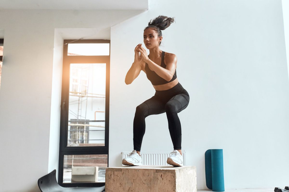 Beautiful sporty woman in sportswear jumping on wooden box in gym. Training, cross fit, sport