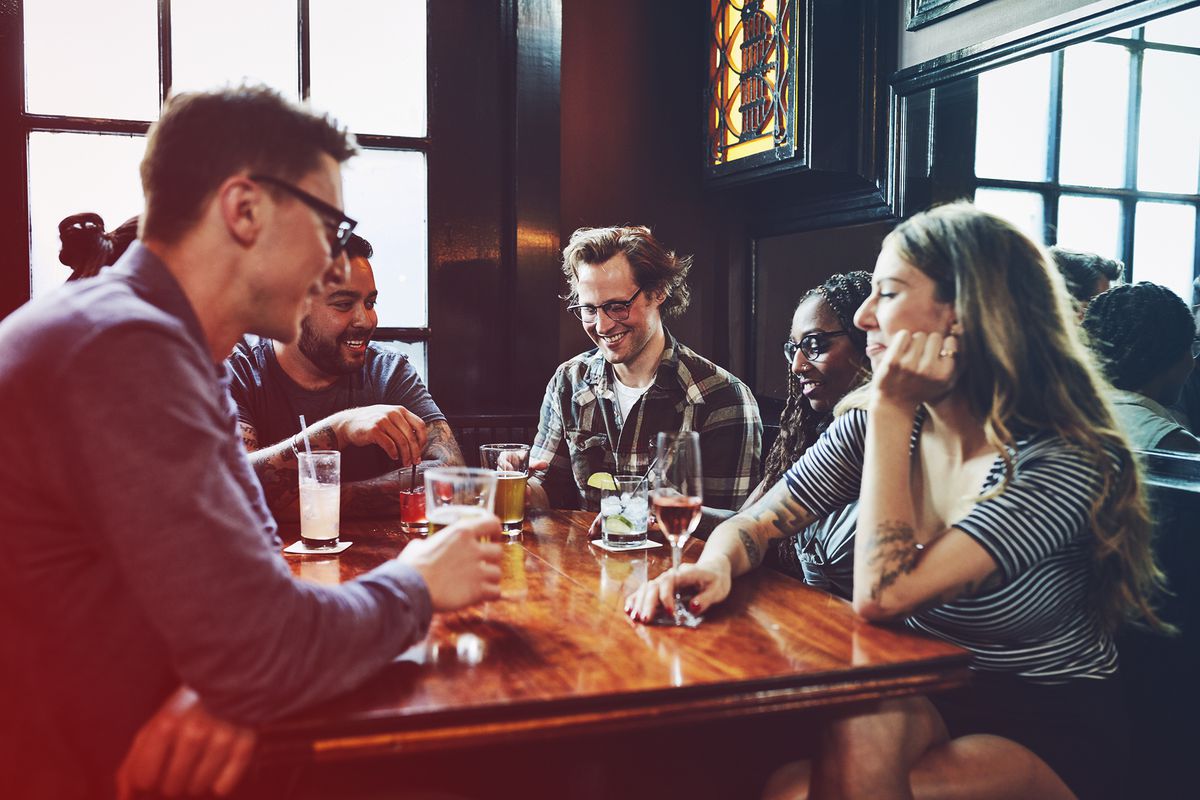 Smiling friends sharing drinks at table in bar , coronavirus-bar-spread