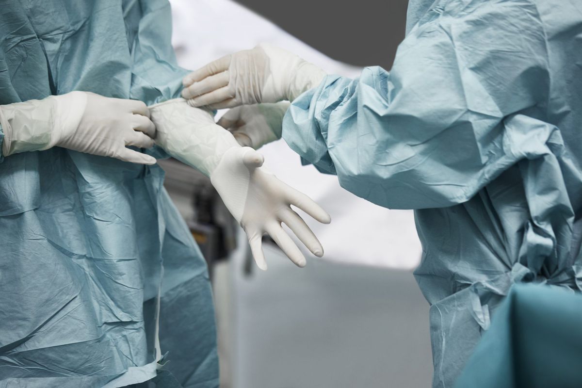 移民大规模子宫切除术，优生学，女医生帮助外科医生戴手术手套上腹部。医学界的同事们正在准备手术。他们站在急诊室里。