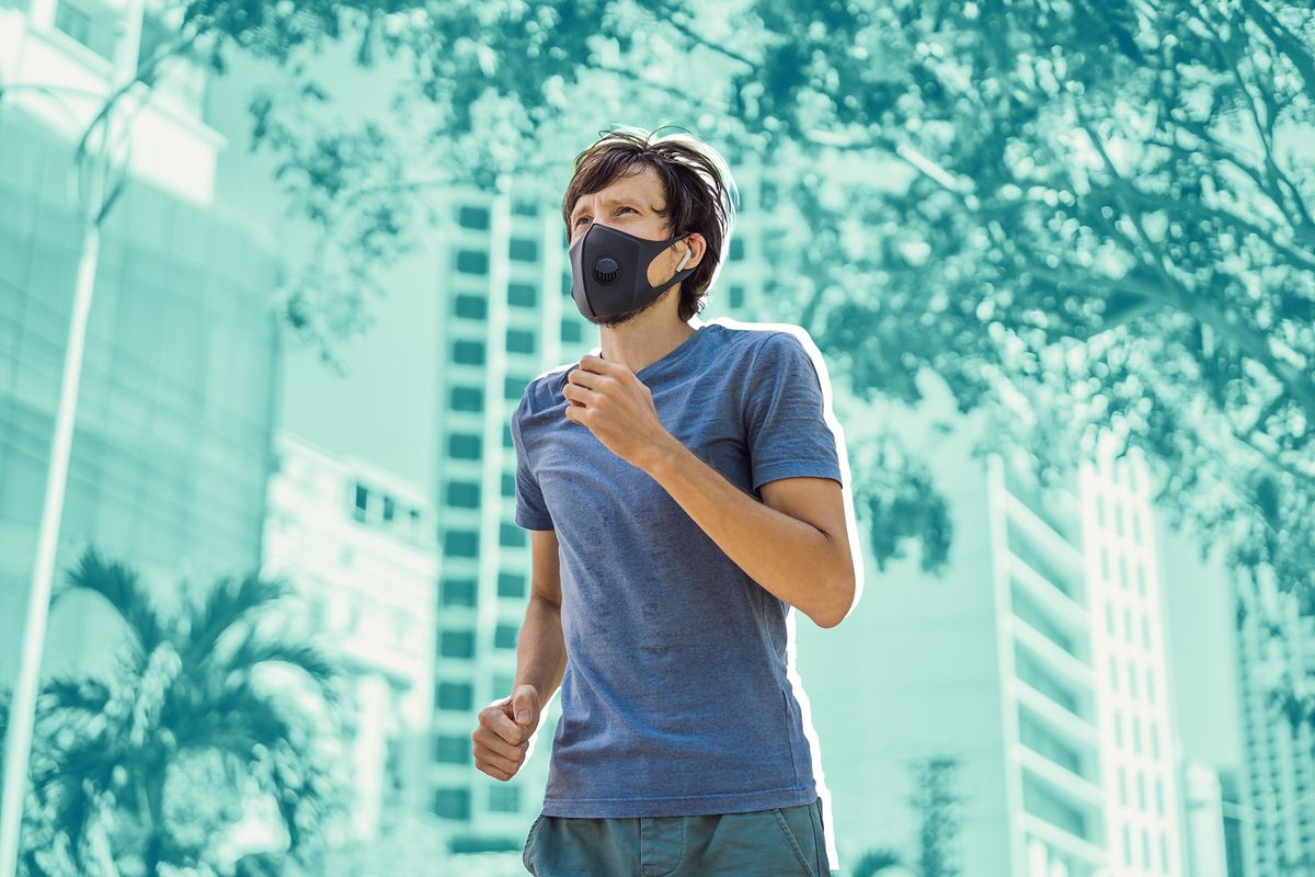 Man runner wearing medical mask. Runningin in the city against the backdrop of the city. Coronavirus pandemic Covid-19. Sport, Active life in quarantine surgical sterilizing face mask protection. Outdoor run on athletics track in Corona Outbreak.