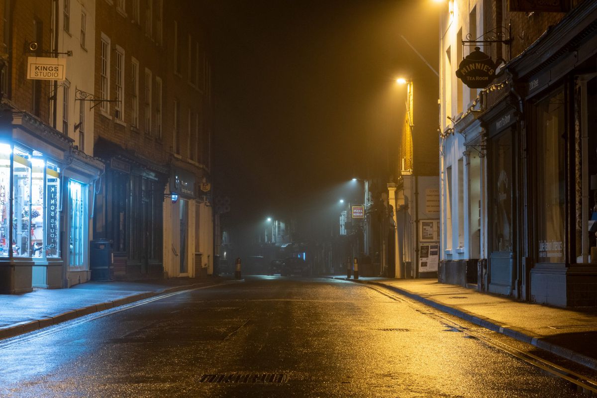pandemic-curfew-efficacy , A wet high street with historic buildings with street lights glowing on a misty winters night. Upton Upon Severn, UKpandemic-curfew-efficacy