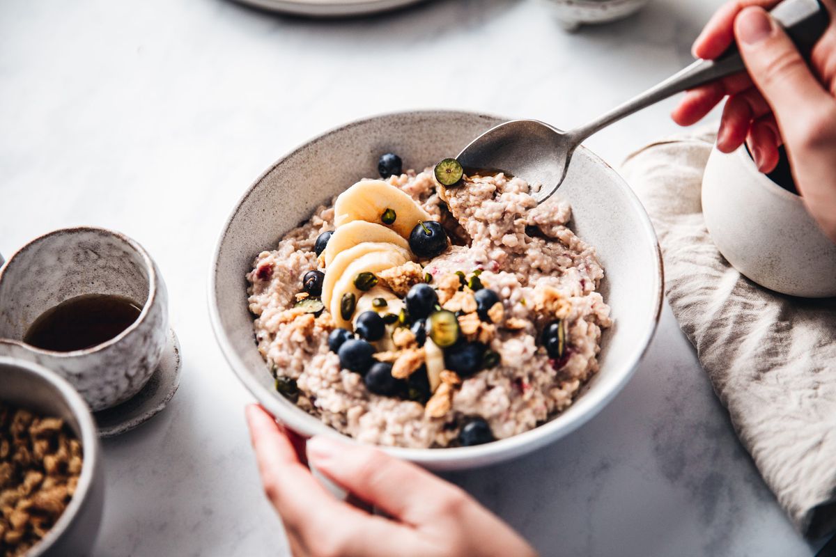 燕麦片是健康的，一个女人把燕麦粉、香蕉和蓝莓混合在一个碗里。女性在厨房做健康早餐。