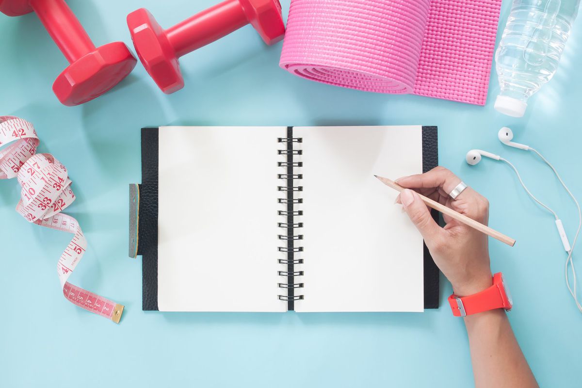 Directly Above Shot Of Cropped Hand Writing In Book On Table , Woman hand holding pencil on blank notebook with sport and Yoga equipments on pastel color background