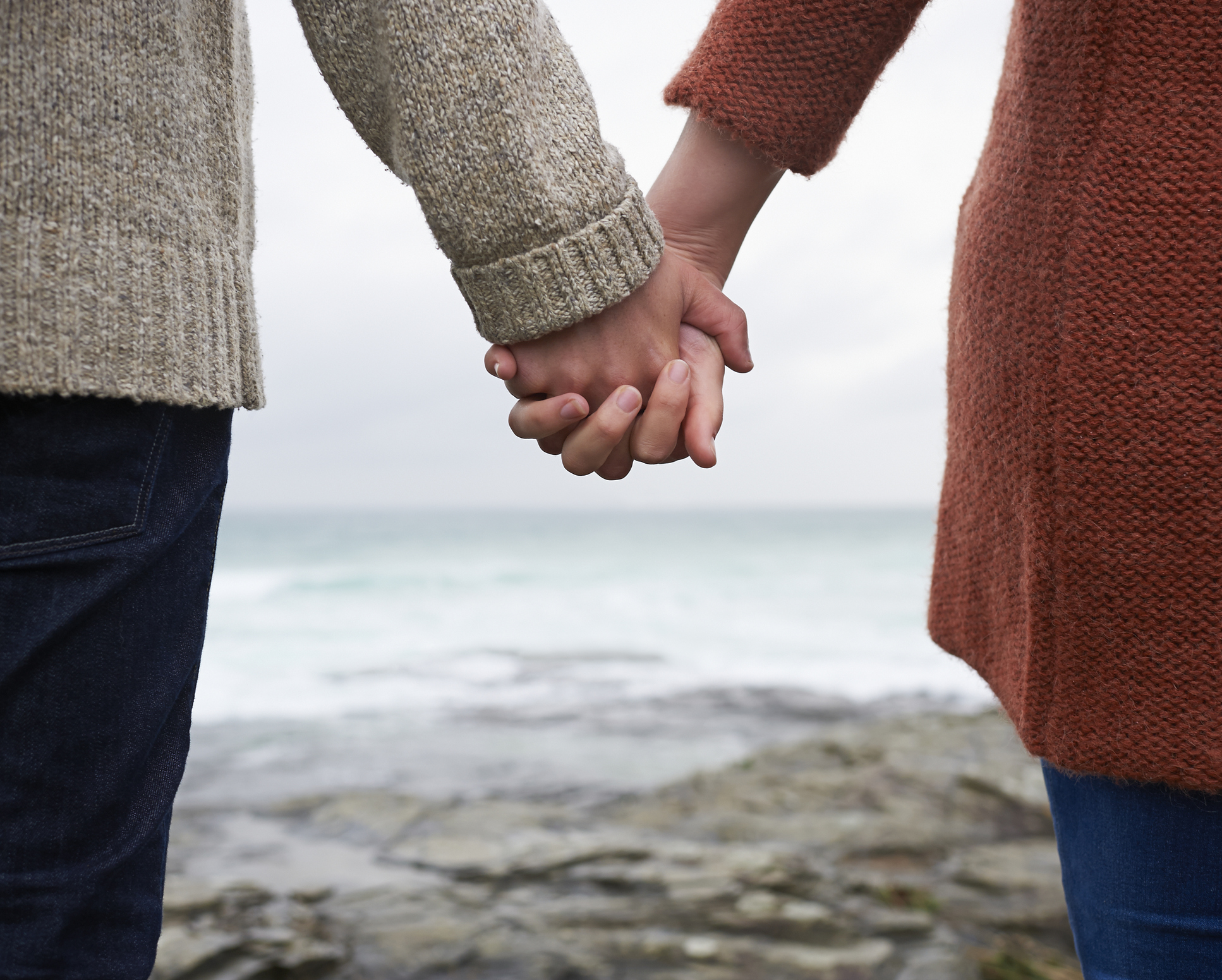 Close up of couple holding hands on coastline.