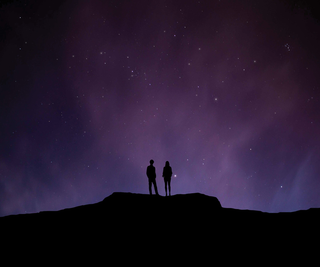 Low Angle View Of Silhouette Man And Woman Standing On Cliff Against Star Field