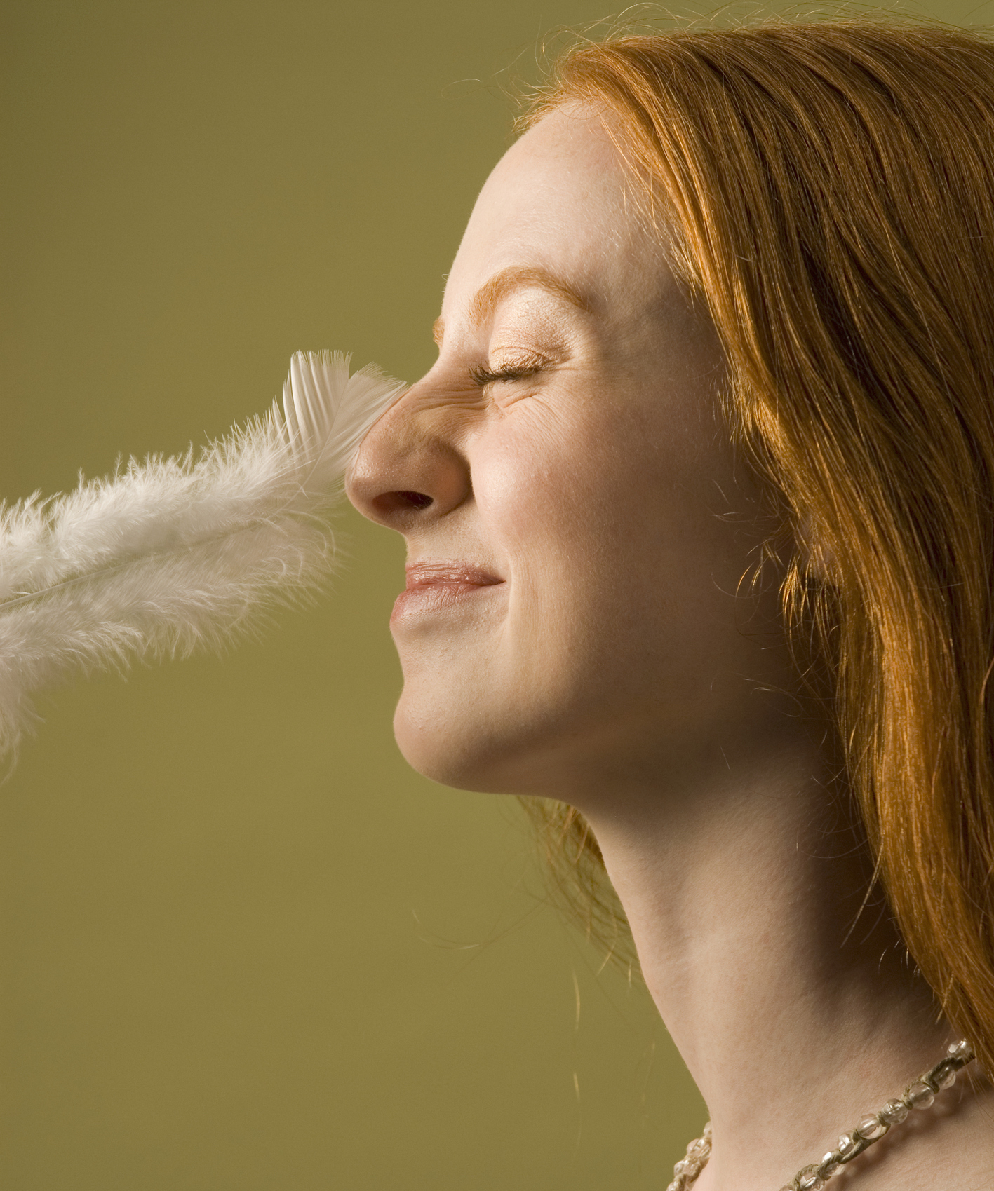 Young woman with nose being tickled by feather, profile
