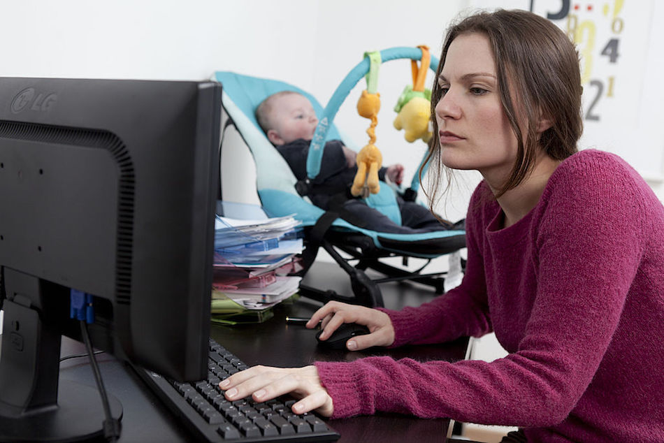 Mom on the computer with her baby in the background