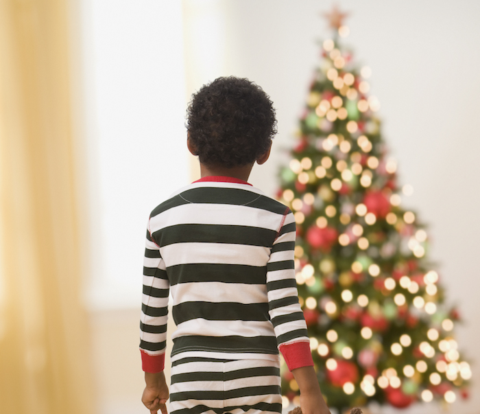 African boy in pajamas with teddy bear looking at Christmas tree