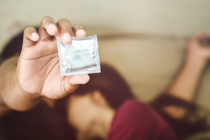 Man and woman in bed, holding condom