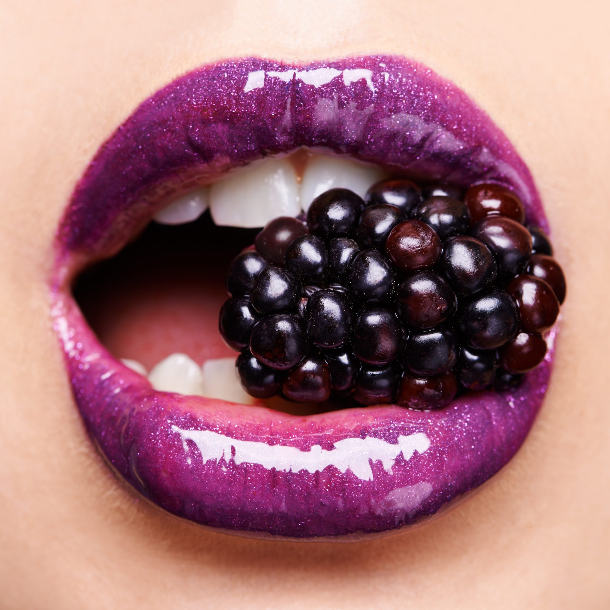 Shot of a woman wearing purple lipstick and biting into a blackberry