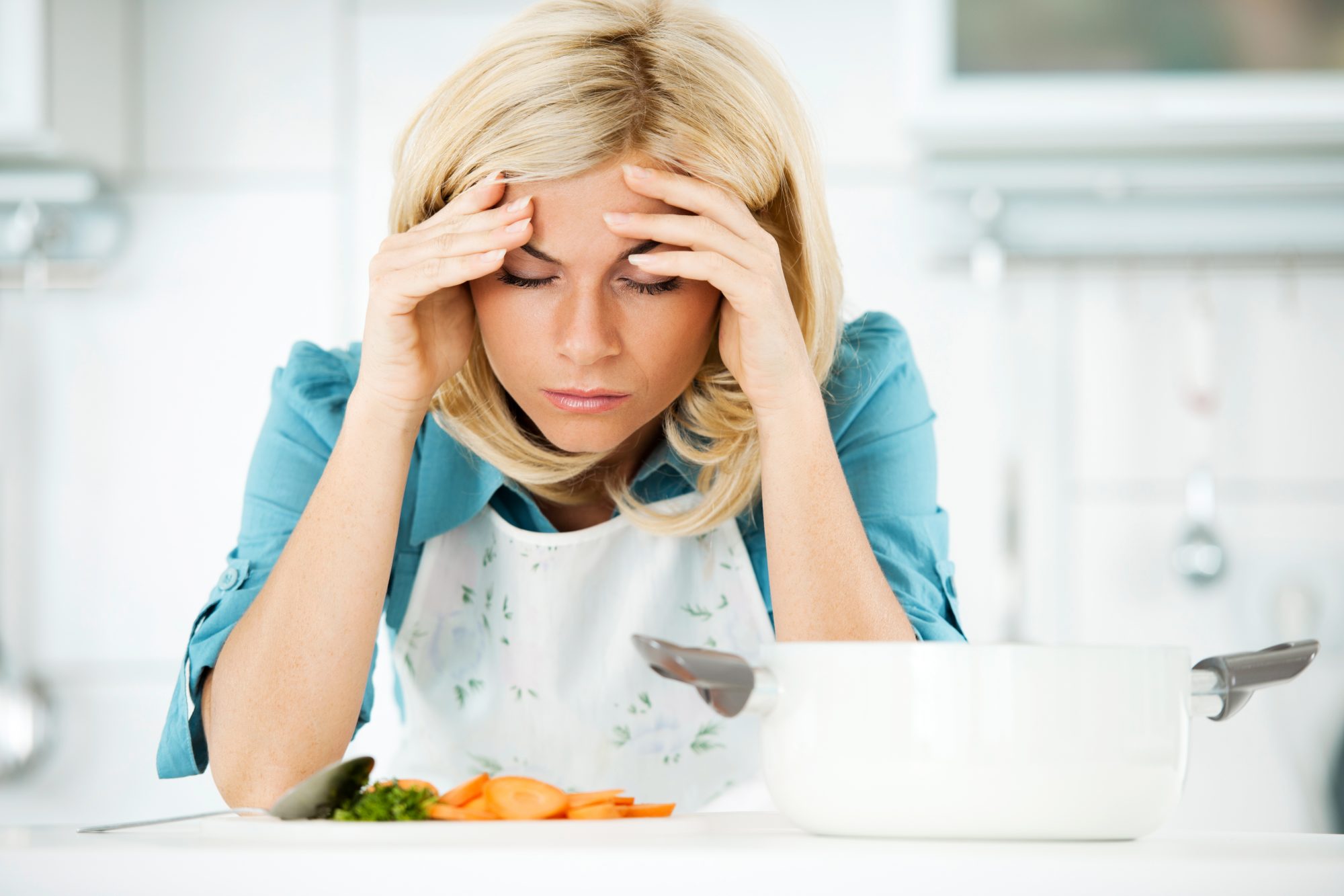 Young blonde housewife having a headache while preparing dinner.