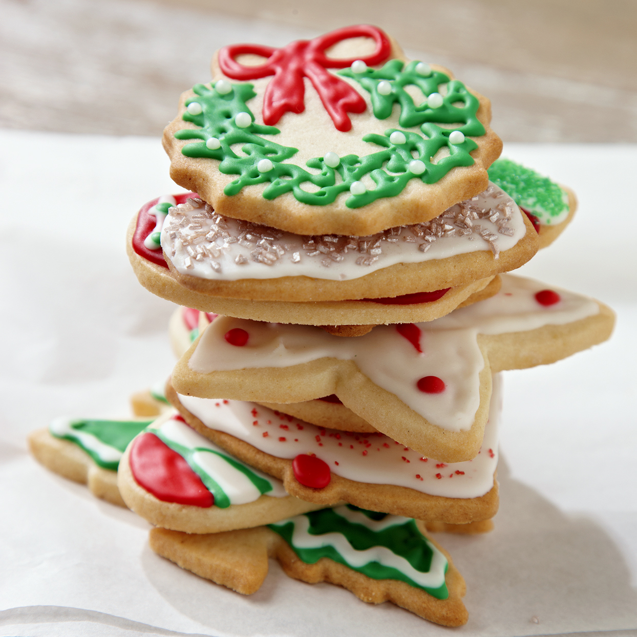Frosted sugar cookies in a stack with a Christmas wreath cookie on top