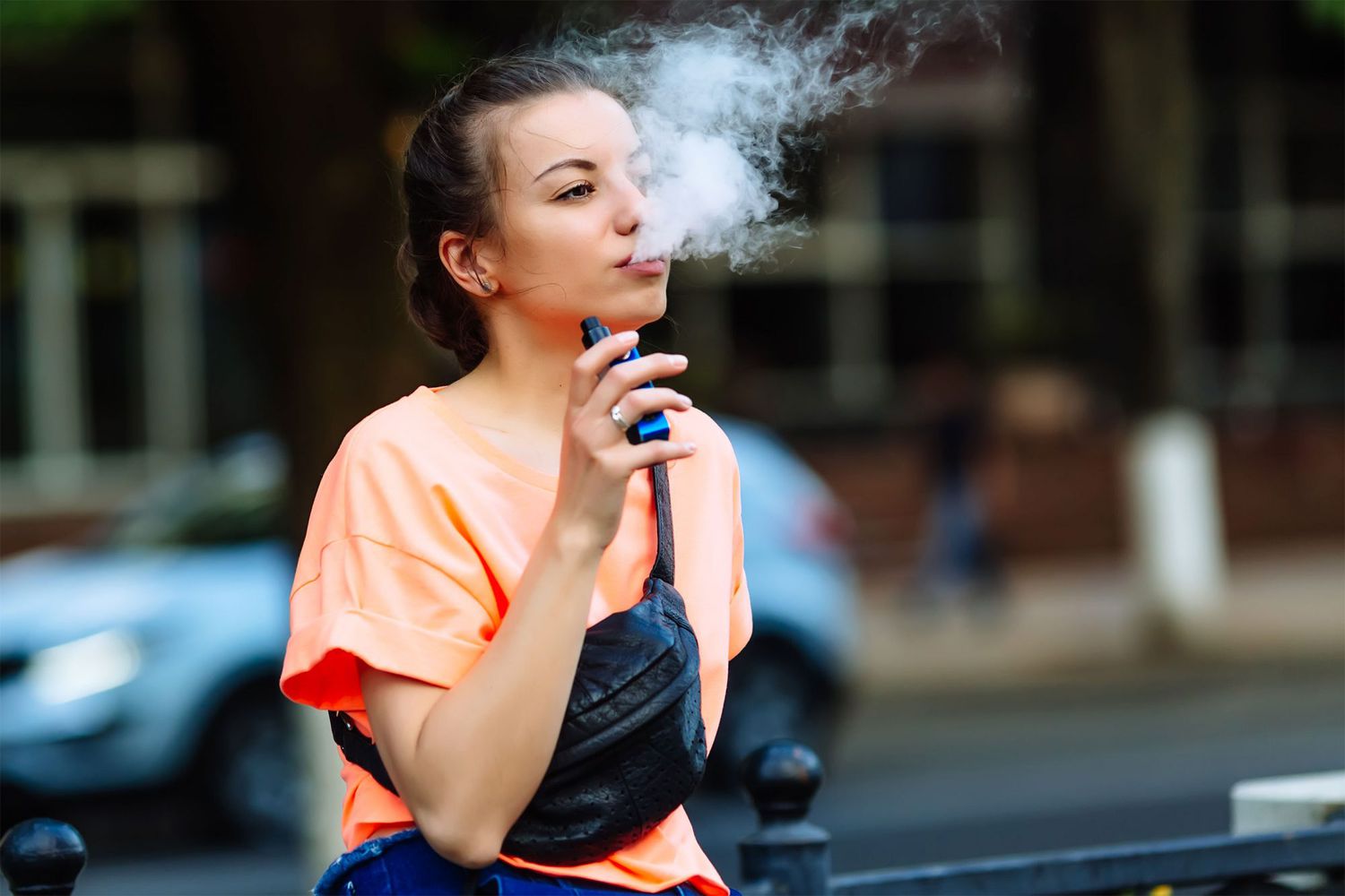 Pretty young hipster woman vape ecig, vaping device at the sunset. Toned image