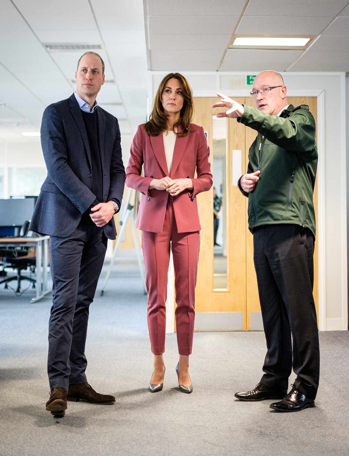 Palace of the Duke and Duchess of Cambridge talking with Chief Executive of the London Ambulance Service, Garrett Emmerson, and an unidentified staff member (left) during a visit to the London Ambulance Service 111 control room in Croydon on Thursday to meet ambulance staff and 111 call handlers who have been taking NHS 111 calls from the public, and thank them for the vital work they are doing.