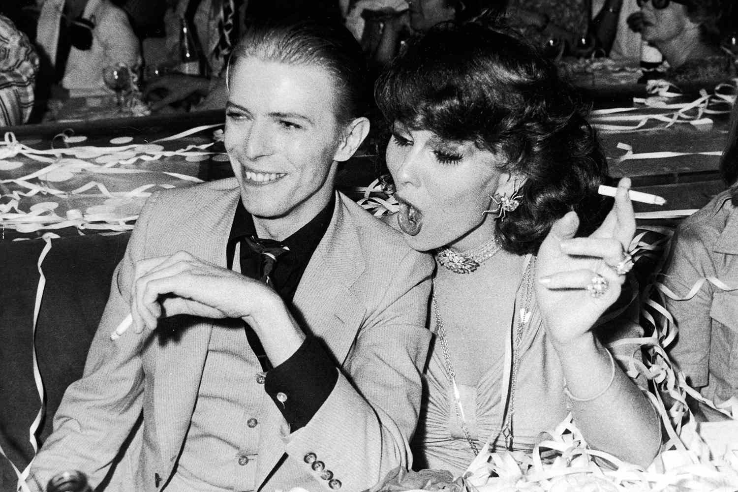 British rock singer and actor David Bowie sits and holds a cigarette with Dutch actor Romy Haag at the club L'Alcazar, following his concert at the Pavilion, Paris, France, May 18, 1976