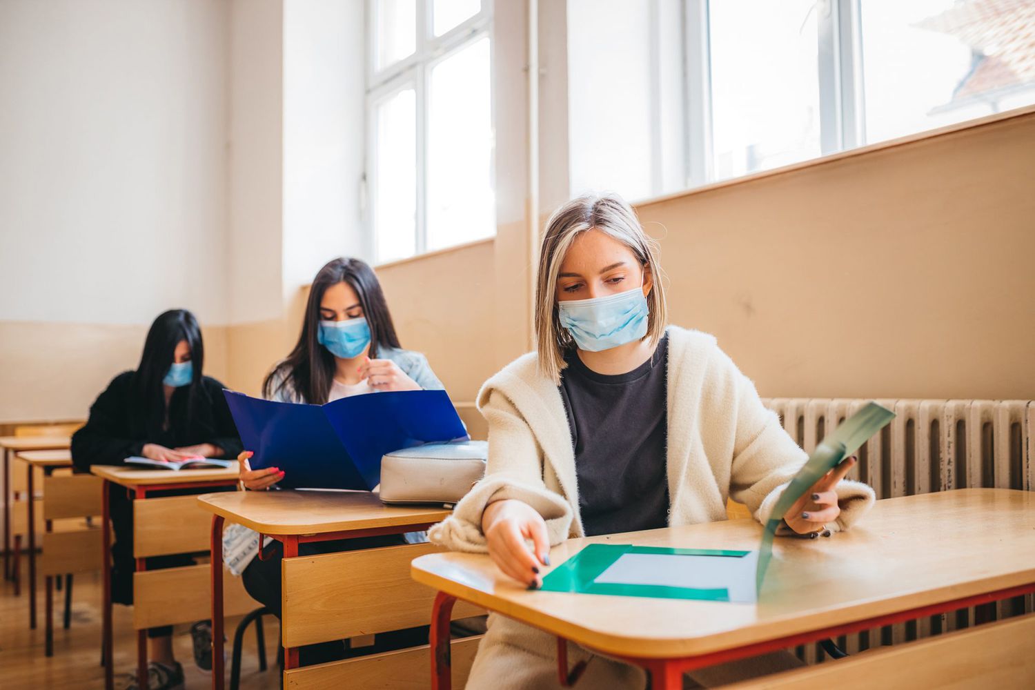 A view of high school students sitting at desks in a classroom with protective masks