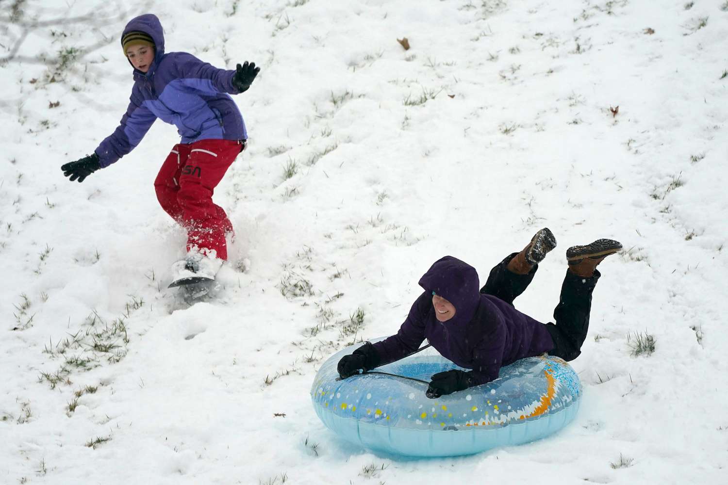 Krystal Krause, right, rides a tube and Lilyann Richard, 11, snowboards down a hill during a snowstorm, in Lutherville-Timonium, Md