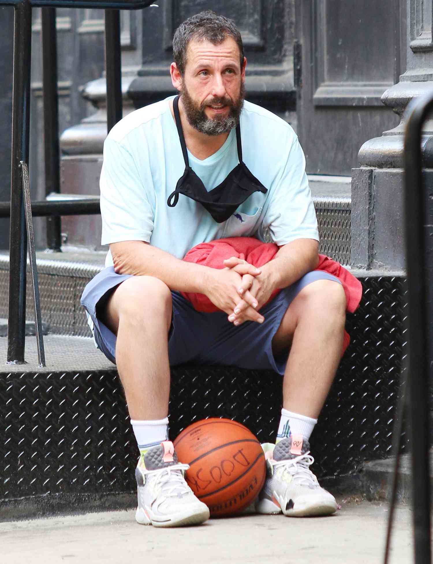 Adam Sandler holds a basketball and sits down to rest after a game in NYC