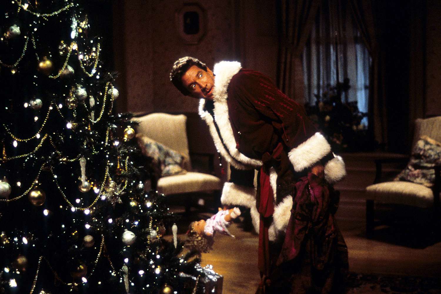 Tim Allen with a doll in his hand, standing next to a Christmas tree in a scene from the film 'The Santa Clause', 1994.
