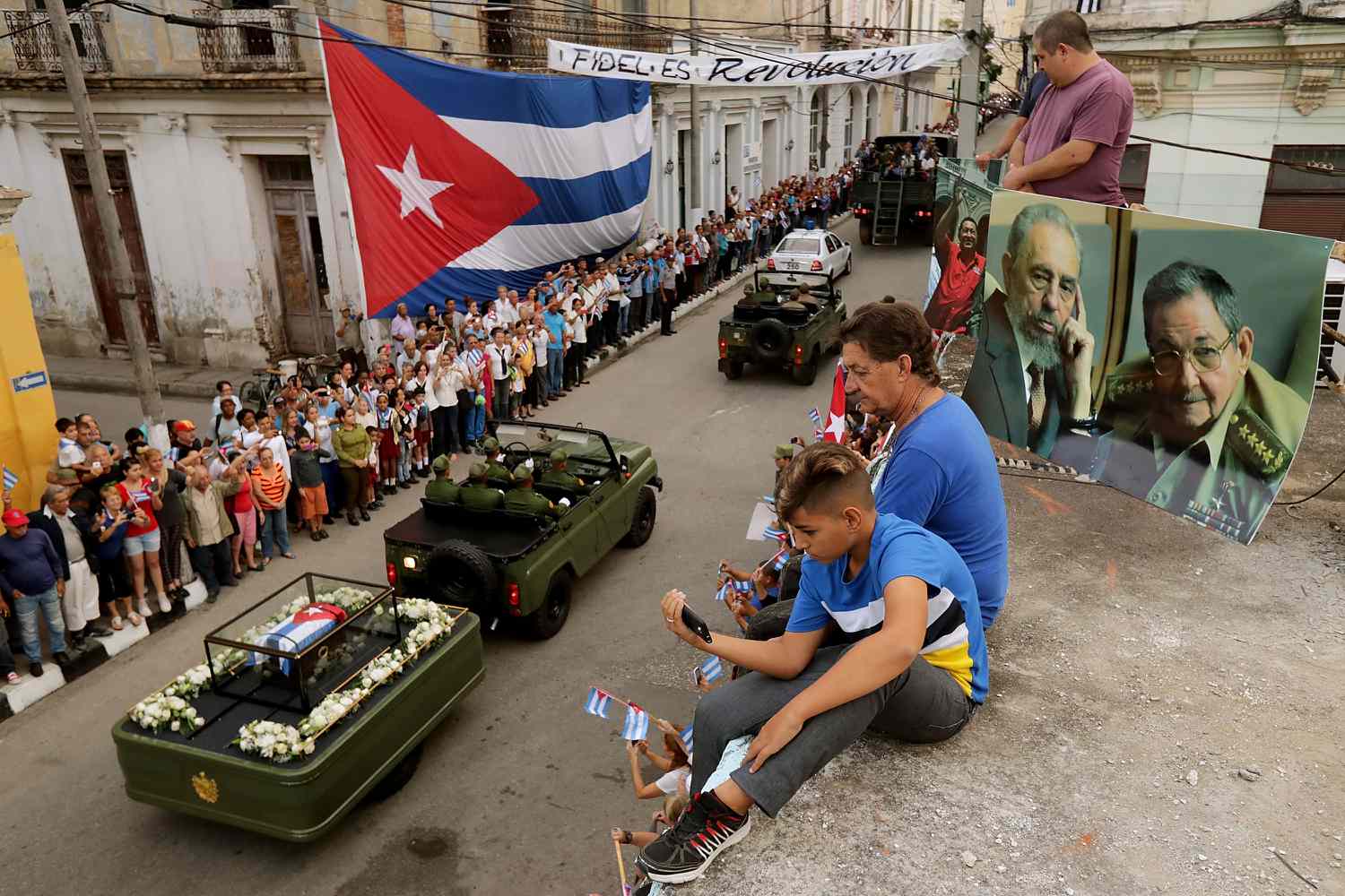 SANTA CLARA, CUBA - DECEMBER 01:  People sit on their rooftop to get a better view as the remains of former Cuban President Fidel Castro pass by on their cross-country journey from Havana to Santiago de Cuba on December 1, 2016 in Santa Clara, Cuba. Castro, the revolutionary leader who brought communism to his island nation in 1959, died November 25 at the age 90 years old.  (Photo by Chip Somodevilla/Getty Images)