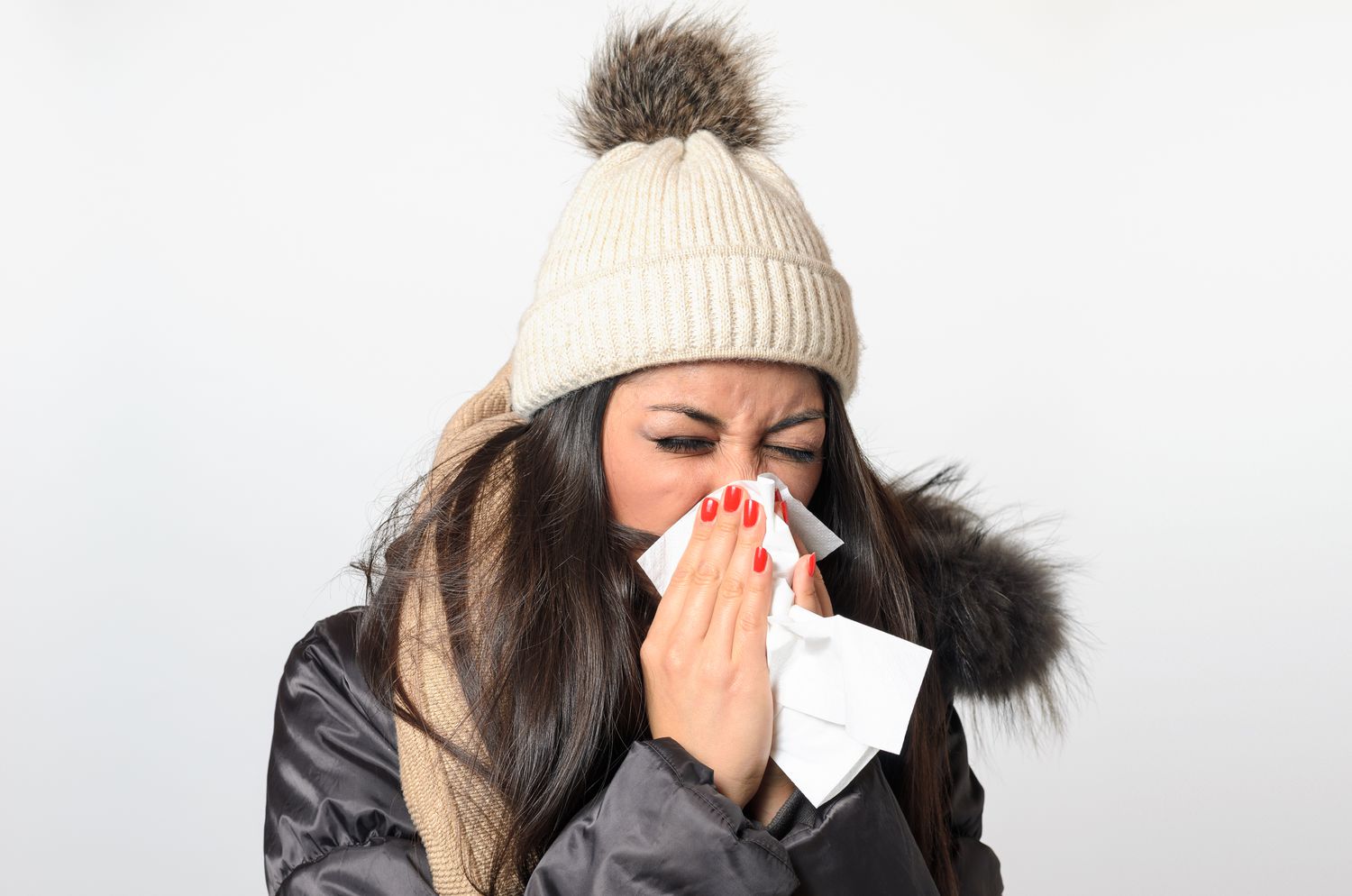 Young Woman In Warm Clothing Blowing Nose Against White Background