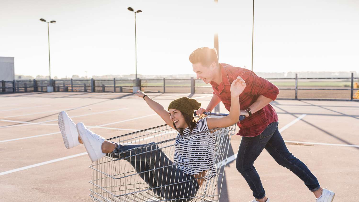 Playful young couple with shopping cart on parking level