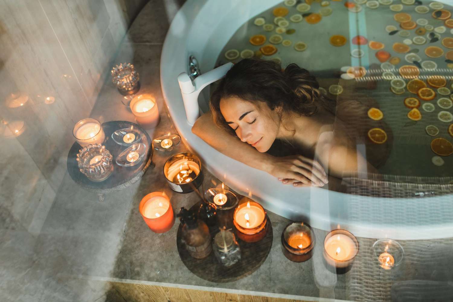 Beautiful young woman relaxing in hot tub-bath with citrus oranges and lemons and with candles.