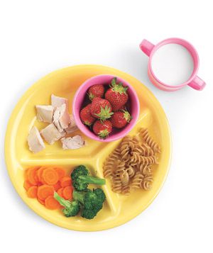 Kid's divided yellow plate with strawberries, chicken, pasta, broccoli, carrots and a glass of milk