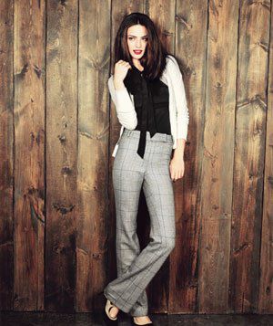 Model wearing tweed plaid pants, white cardigan, black blouse with bow and two-tone suede heels