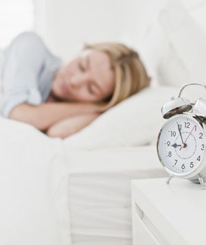 Woman sleeping next to an alarm clock on bedside table