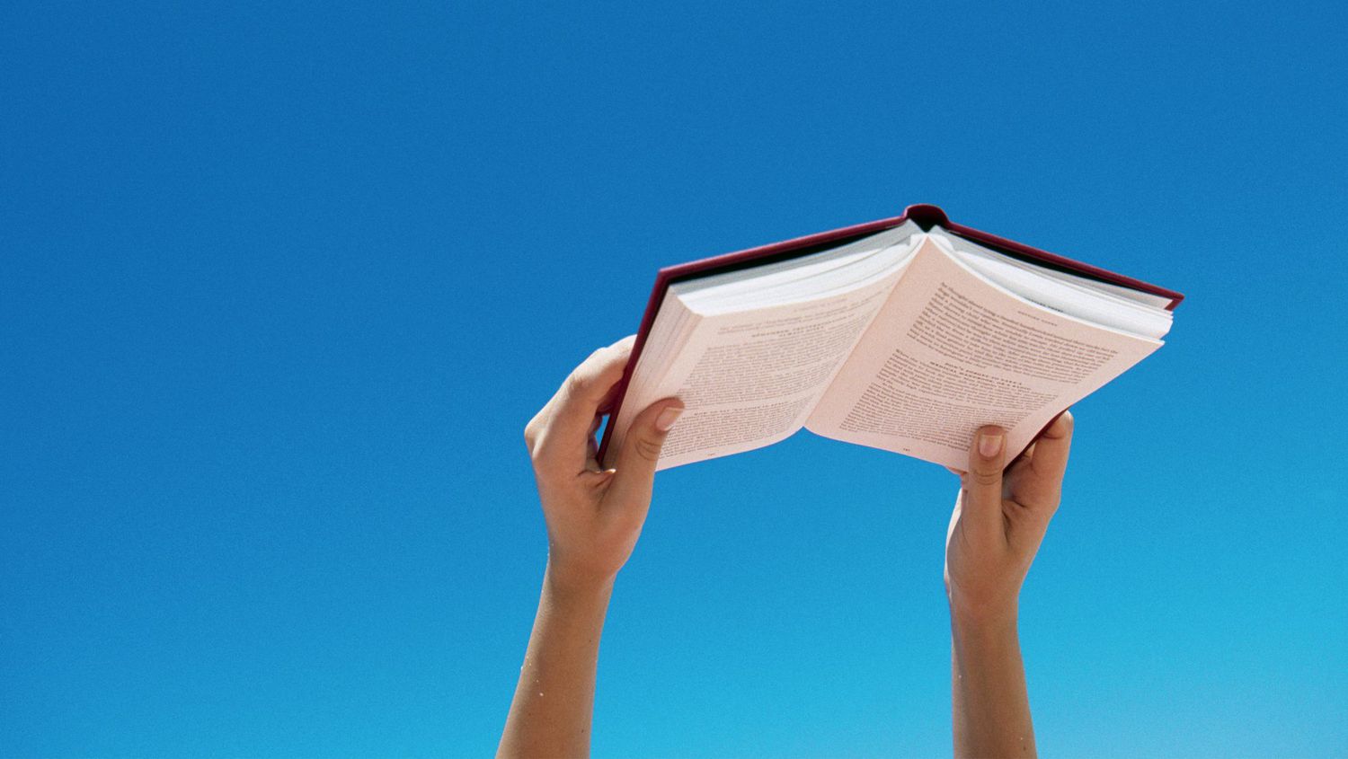 Close up of person's hands holding books against a blue sky