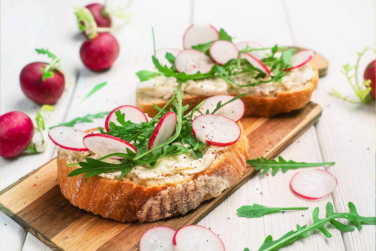 Toast topped with radish slices and arugula sitting on table with radishes