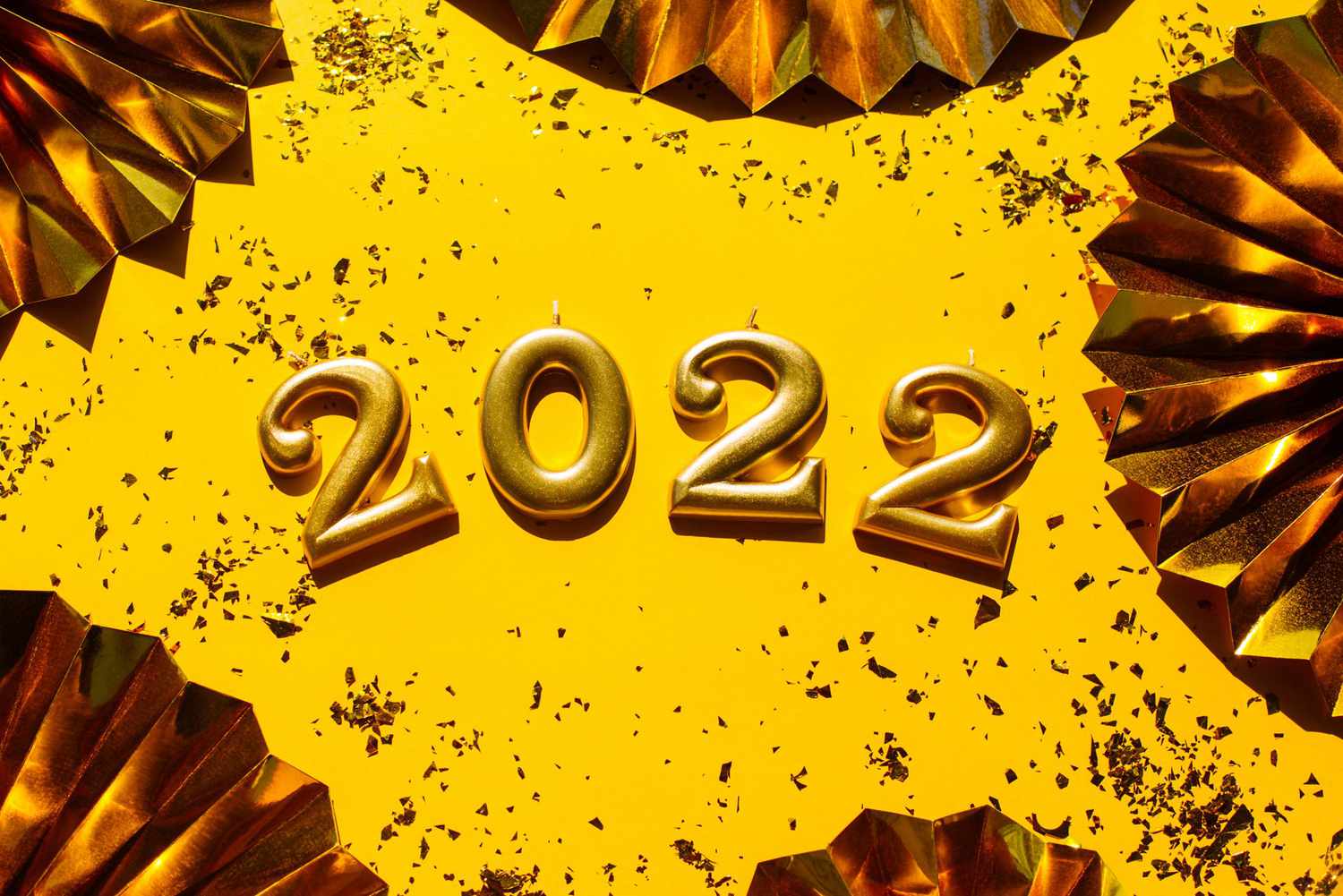 From above composition with 2022 number on bright yellow surface with golden glitter stars and scattered spangles for New Year holiday decorations