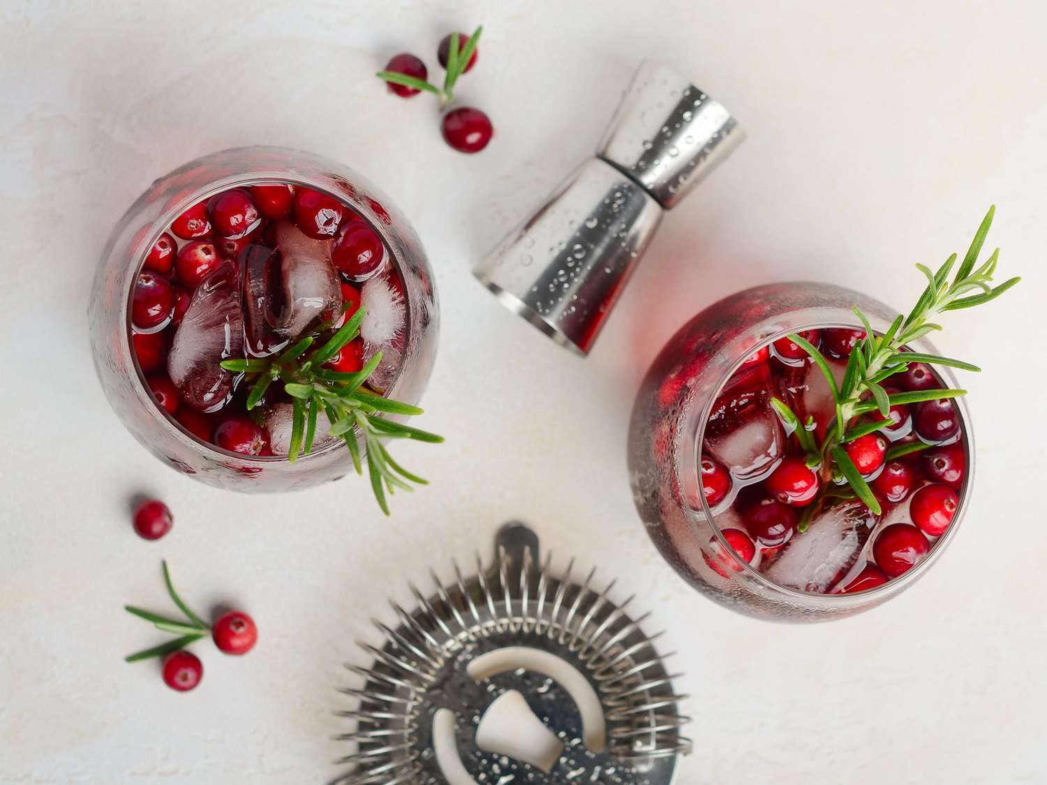 Cold refreshing drink with cranberries and rosemary on a white concrete background