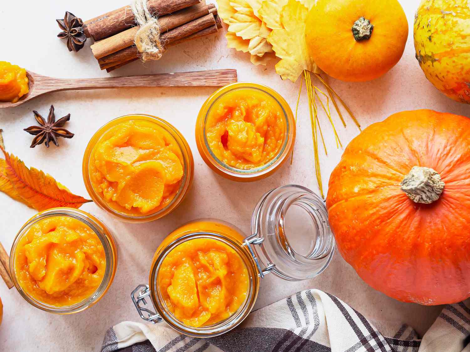 Pumpkin puree in different glass jars with spices and fresh pumpkins. Autumn or winter food. Light stone background. Top view.