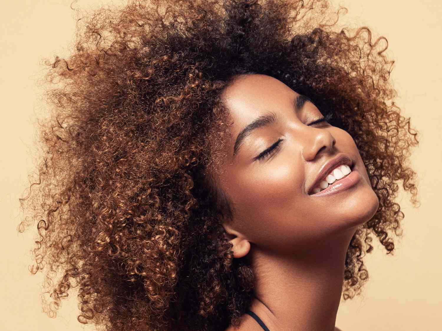 Natural Afro brown hair. Wide toothy smile and expression of gladness on the face of young brown skinned woman. Afro beauty.
