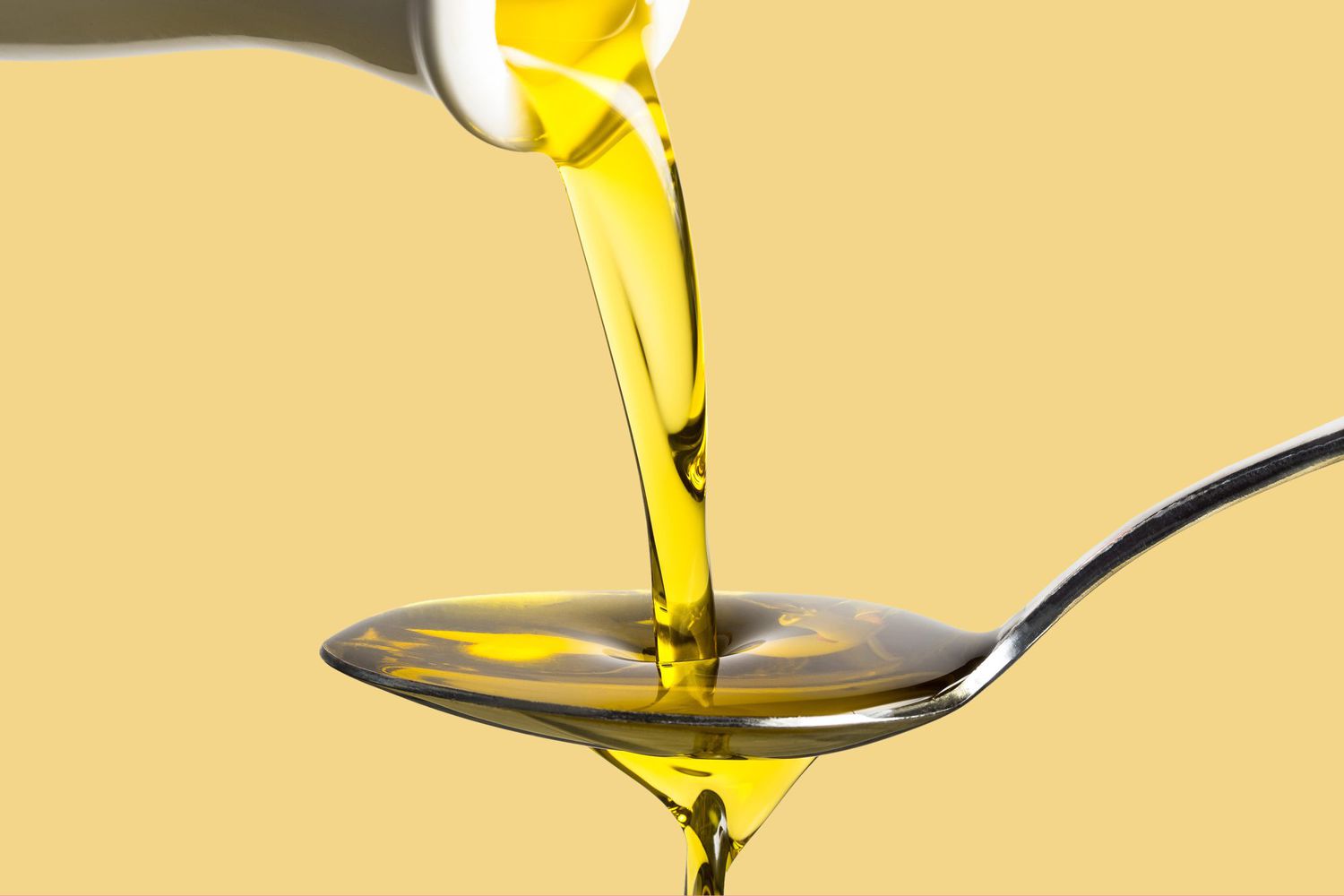 Cooking oil being poured onto a spoon on a yellow background