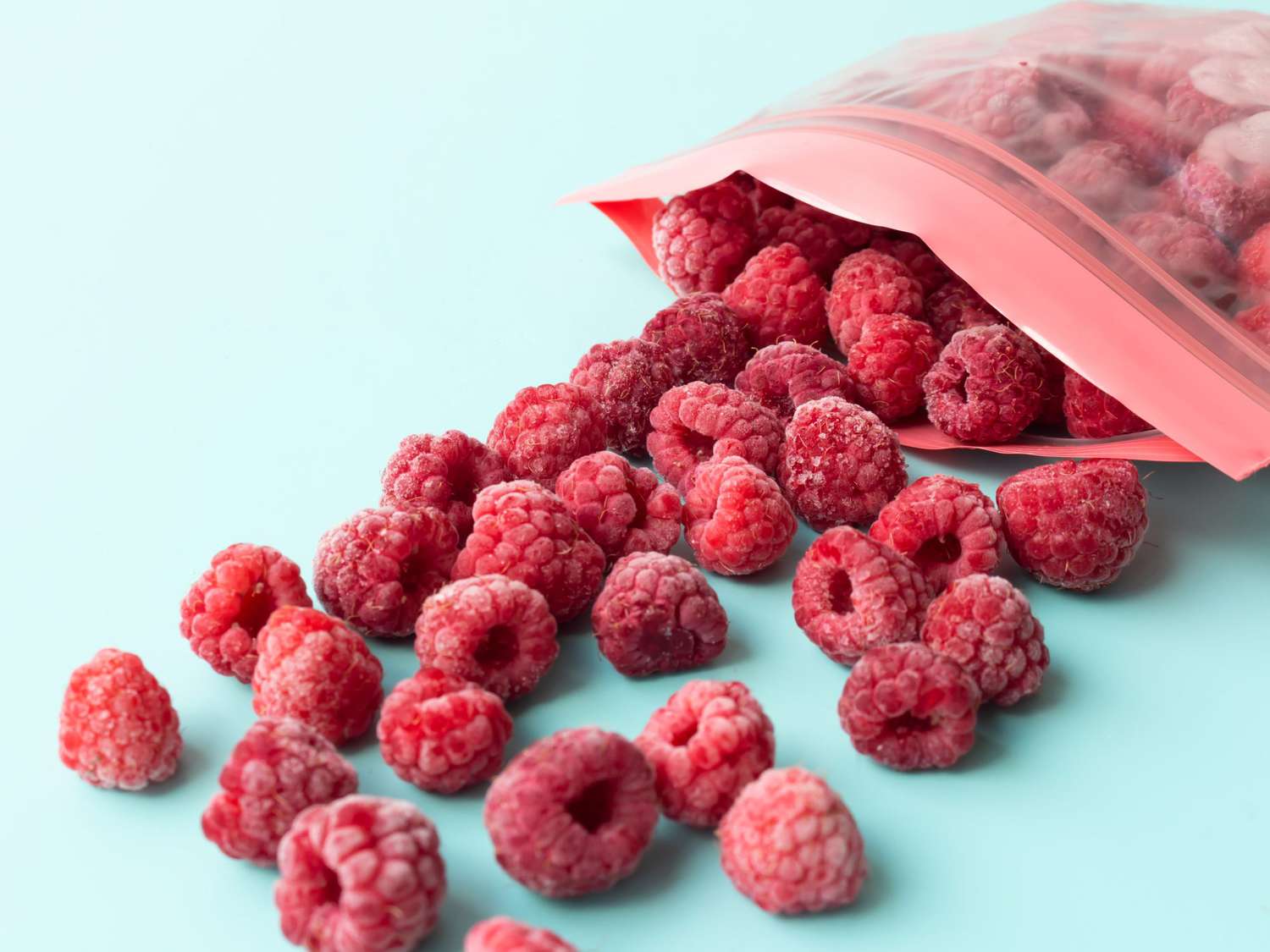 Frozen raspberries in a plastic bag with a fastener on a blue background.